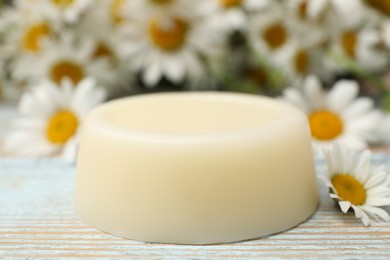 Solid shampoo bar and chamomiles on light wooden table, closeup. Hair care
