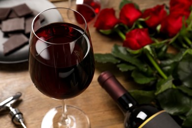 Glass of red wine near beautiful roses on wooden table, closeup