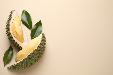 Pieces of fresh ripe durian and leaves on beige background, flat lay. Space for text