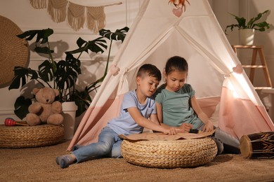 Photo of Cute little children with treasure map near toy wigwam at home