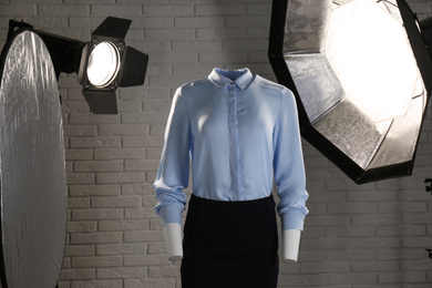 Stylish clothes on ghost mannequin and professional lighting equipment in modern studio. Fashion photography