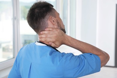 Photo of Exhausted doctor rubbing his neck in hospital, back view