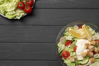 Bowl of delicious salad with Chinese cabbage, lemon, tomatoes and bread croutons on black wooden table, flat lay. Space for text