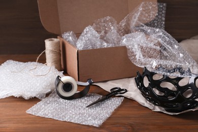Beautiful ceramic bowl with bubble wrap near cardboard box and packaging materials on wooden table