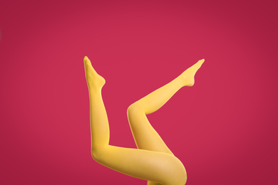 Woman wearing yellow tights on crimson background, closeup of legs