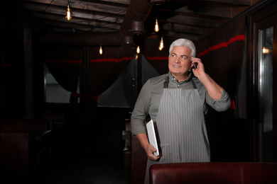 Senior business owner talking on phone in his restaurant