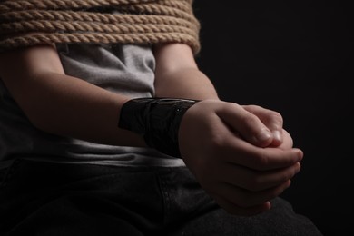 Photo of Little boy tied up and taken hostage on dark background, closeup