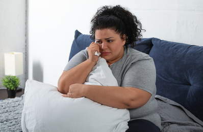 Depressed overweight woman crying while hugging pillow on bed