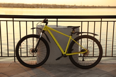 Yellow bicycle parked near railing on city waterfront at sunset