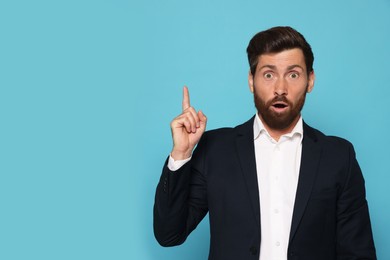 Surprised bearded man pointing index fingers up on light blue background. Space for text