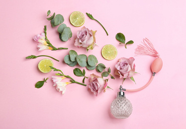 Beautiful flat lay composition with bottle of perfume, lime, eucalyptus and flowers on pink background