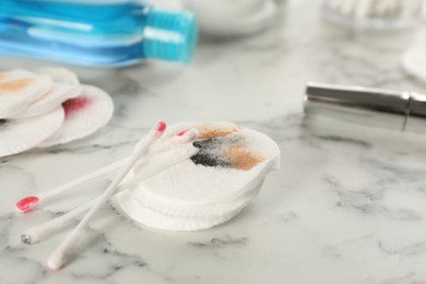 Dirty cotton pads, swabs and makeup removal product on white marble table, closeup