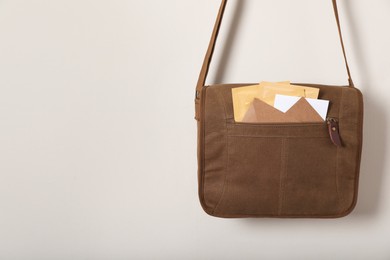 Brown postman bag with mails hanging on light wall, space for text