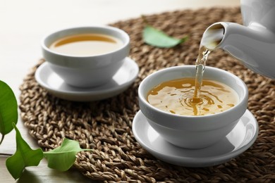 Photo of Pouring green tea into white cup with saucer on table, closeup