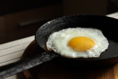 Frying pan with tasty cooked egg on wooden board, closeup