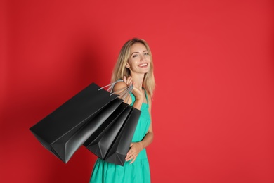 Happy young woman with shopping bags on red background, space for text. Black Friday Sale