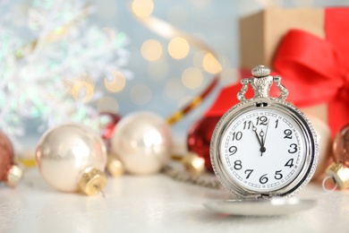 Pocket watch, gift and festive decor on table against blurred lights. New Year countdown