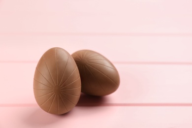 Sweet chocolate eggs on pink wooden table. Space for text