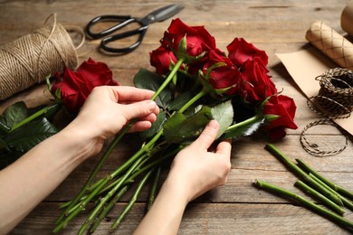 Photo of Woman making luxury bouquet of fresh roses at 
 wooden table, closeup
