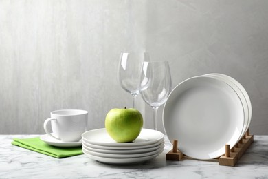 Set of clean dishware, glasses and apple on white marble table