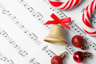 Photo of Golden shiny bell with red bow, candy canes and Christmas baubles on music sheets, flat lay and space for text