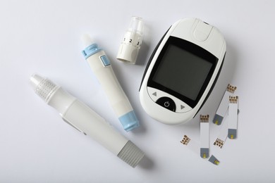 Digital glucometer, lancet pens and test strips on white background, flat lay. Diabetes control