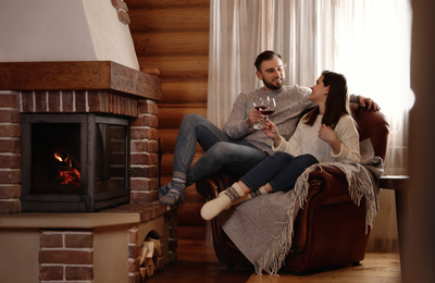 Lovely couple with glasses of wine resting near fireplace at home. Winter vacation