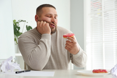 Lazy overweight office employee with donut at workplace