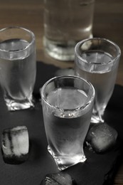 Shot glasses of vodka with ice cubes on table, closeup