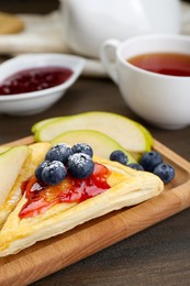 Photo of Fresh tasty puff pastry with jam, blueberries and pear on wooden table, closeup