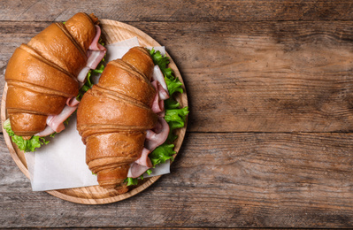 Tasty croissant sandwiches with ham on wooden table, top view. Space for text