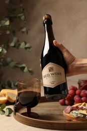 Photo of Woman holding bottle of red wine over table with different snacks, closeup