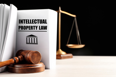 Intellectual Property law book, judge's gavel and scales of justice on white table against black background. Space for text