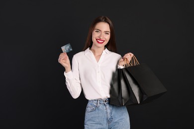 Photo of Happy young woman with shopping bags and credit card on black background. Big sale