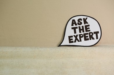 Paper message bubble with phrase Ask The Expert near beige wall, space for text