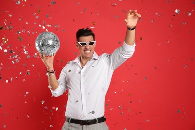 Happy man with disco ball and confetti on red background