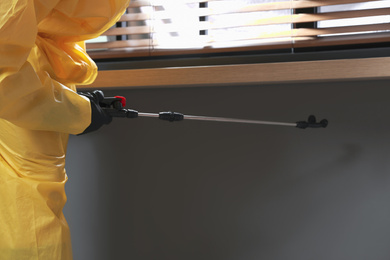 Pest control worker in protective suit spraying insecticide on window sill indoors, closeup