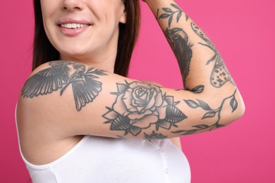 Photo of Beautiful woman with tattoos on arm against pink background, closeup