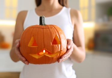 Woman holding pumpkin jack o'lantern indoors, closeup. Halloween celebration