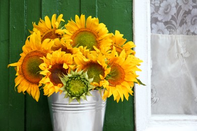 Photo of Bouquet of beautiful sunflowers in bucket near window outdoors