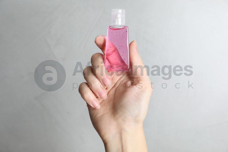 Woman holding antiseptic gel on light grey background, closeup