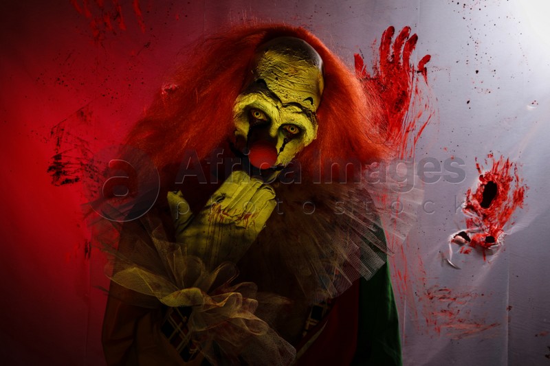 Photo of Terrifying clown against bloodstained plastic film. Halloween party costume