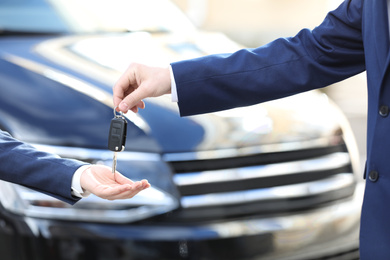 Salesman giving key to customer in modern auto dealership, closeup. Buying new car