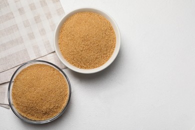Brown sugar in bowls on white table, flat lay. Space for text