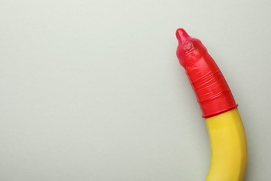 Banana with condom on light grey background, top view and space for text. Safe sex