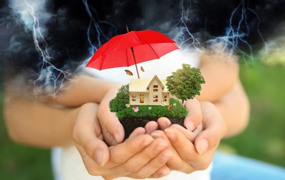 Insurance concept - umbrella demonstrating protection. Family holding house model with green lawn, closeup