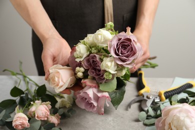 Florist creating beautiful bouquet at grey table against light background, closeup