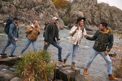 Photo of Group of friends with backpacks crossing mountain river on autumn day