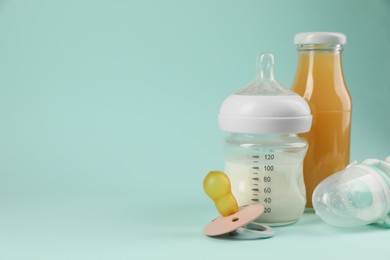 Photo of Milk, juice, pacifier and nibbler on light blue background, space for text. Baby nutrition