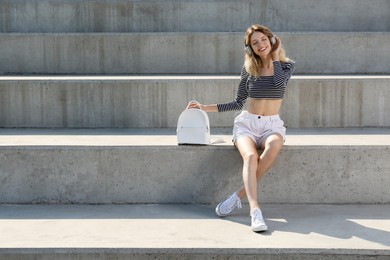 Young woman with stylish backpack on stairs outdoors. Space for text